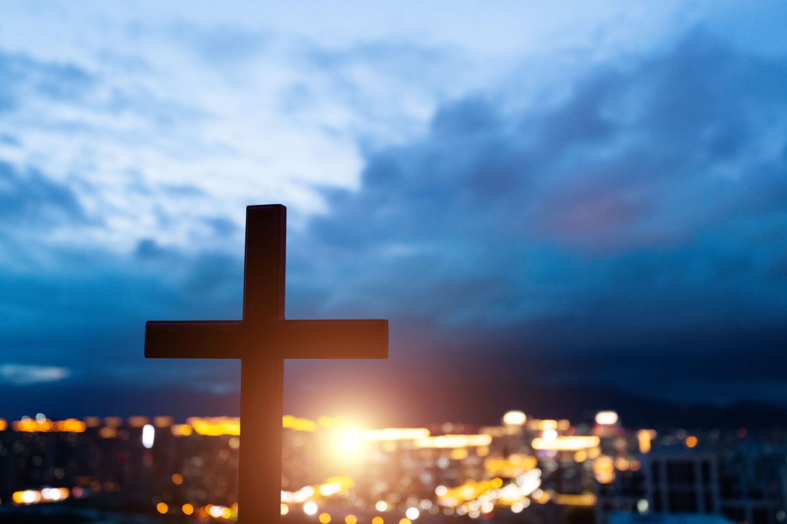 Silhouette of cross against cityscape at dusk.